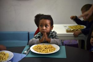 Priorities: A young boy prays before tucking in to some food at the shelter